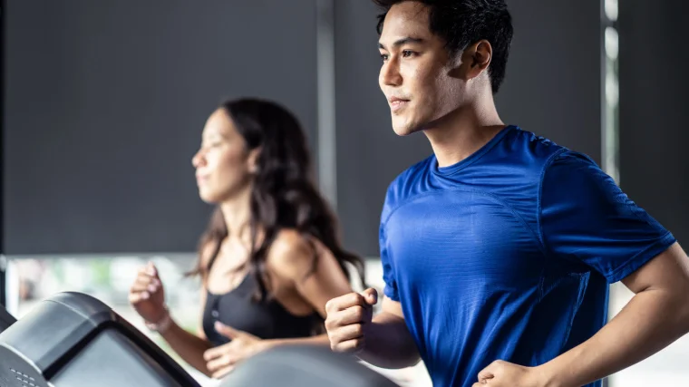 Two athletes run next to each other on treadmills at the gym.