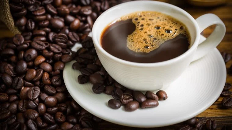 A cup of coffee with coffee beans around it.