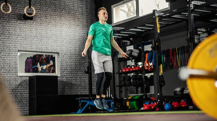 A person wearing a bright green shirt performs double unders in a functional fitness gym area.