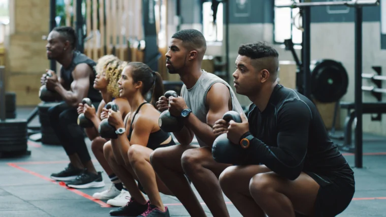 A group of athletes doing kettlebell squat exercise.