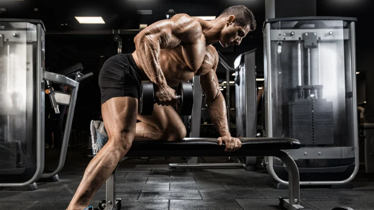 A muscular person performing dumbbell row in the gym.