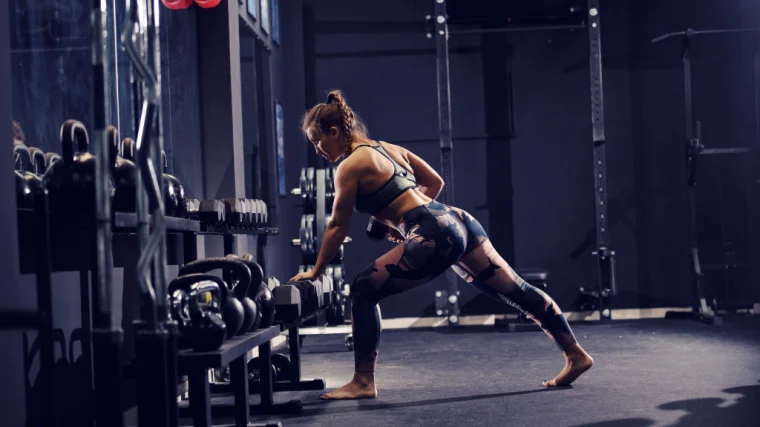 woman performs dumbbell row leaning against rack
