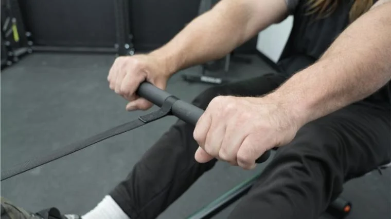 A person gripping the handlebar of the YOSUDA Water Rowing Machine.