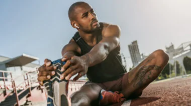 Sporty,Muscular,African,Male,Athlete,In,Earphones,Looking,Away,,Stretching