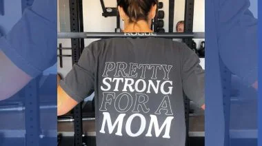 A woman works out with a shirt that reads "Pretty strong for a mom".