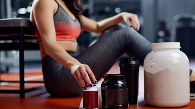 Person sitting in a gym with supplement containers and a shaker bottle near them