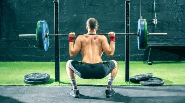 Back view of a sportsperson lifting a barbell in the gym.