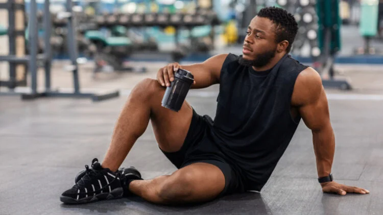 A person sits down in the gym and sips from a water bottle.