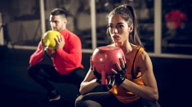 Two people lifting kettlebells while squatting in the gym