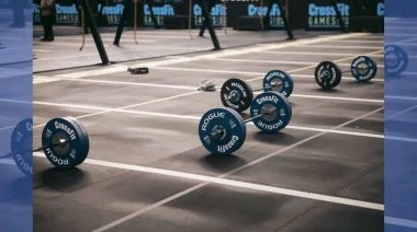 An assortment of barbells are scattered across the mats at a CrossFit competition