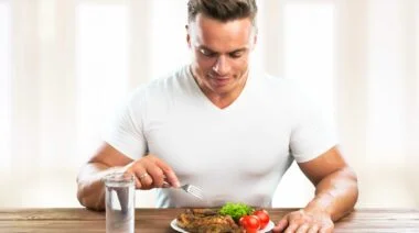 A bodybuilder getting ready to eat grilled chicken set on a plate.