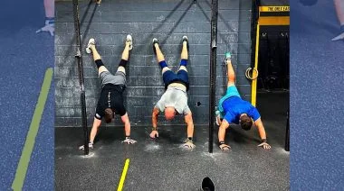 Three CfrossFit athletes doing handstands against a wall.