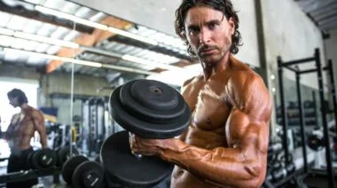 A bodybuilder doing alternate dumbbell curls in the gym.