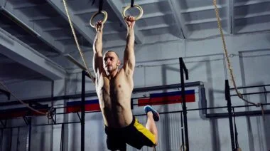 Man in yellow shorts and no t-shirt doing muscle-ups on a pair of rings.