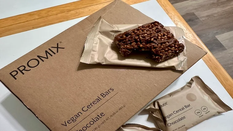An opened Promix Protein Puff Bar rests on the box.