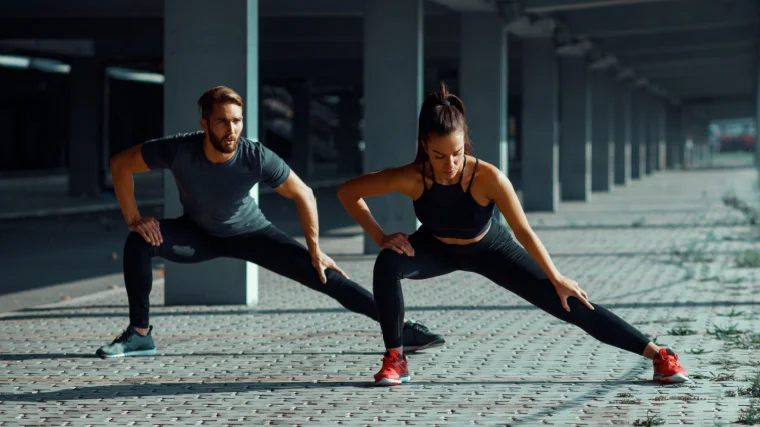 Two fit individuals stretching their legs outdoors.
