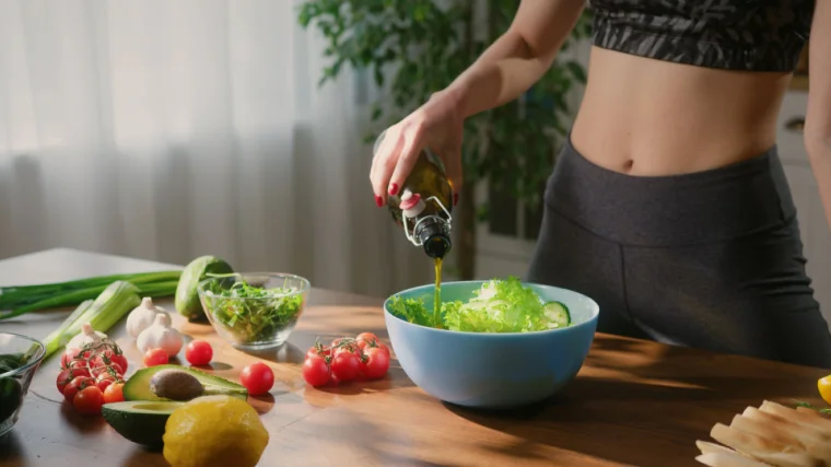 A person adding olive oil on fresh vegetable salad.