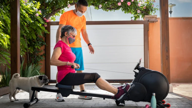 A person with their personal trainer doing rowing exercise on a rowing machine.