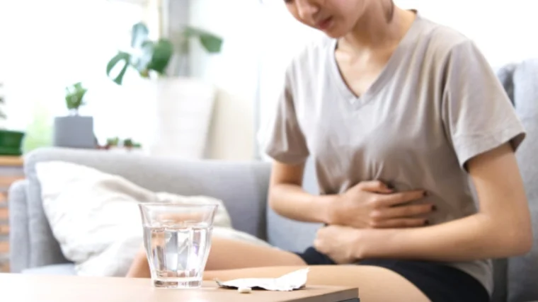 A person having cramps during their monthly period, and a glass of water on the table.