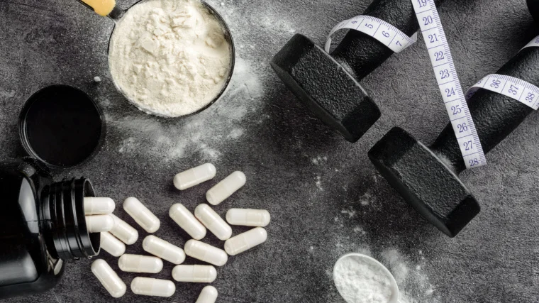 Protein and BCAA powder in scoops next to a set of dumbbells and measuring tape.