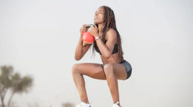 A person performs a kettlebell goblet squat on a beach.