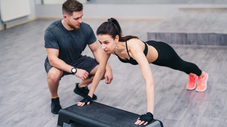 A person being coached in the gym while doing in inclined push-up.