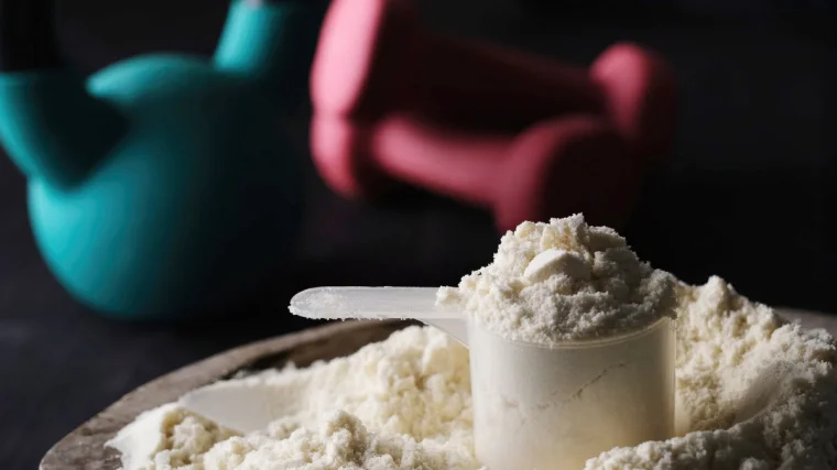 Protein powder in a scoop, with free weights in the background.