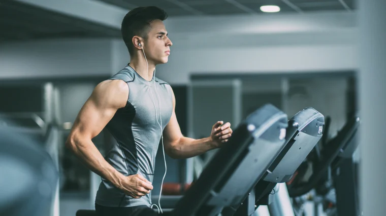 A person wears a grey tank top while running on a treadmill.