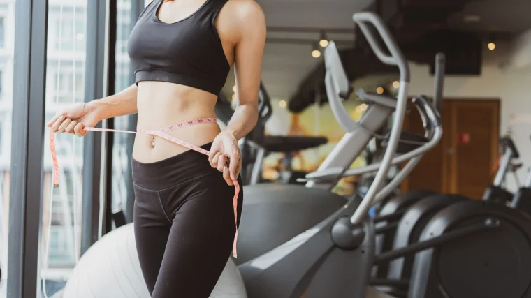 A fit person measuring waist size with a measuring tape.