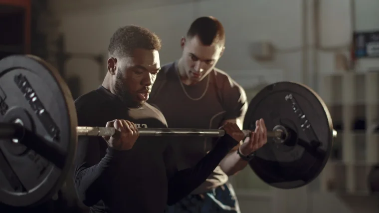 A person working out with a barbell and being coached.