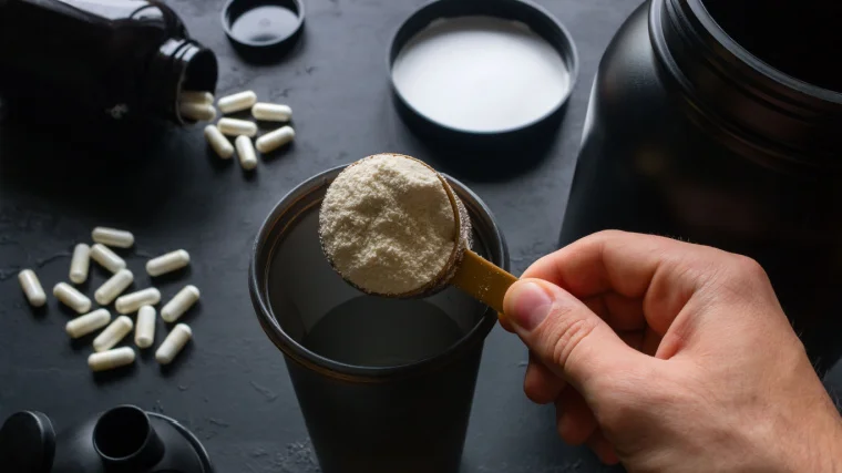 A person pouring powdered supplement in a shaker.