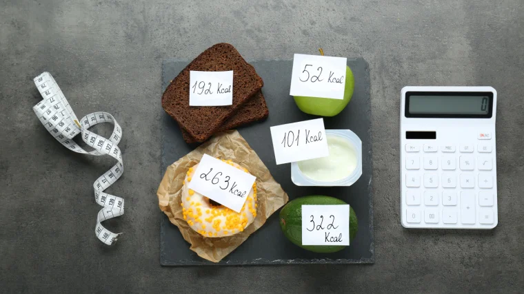 A measuring tape, calculator, and food products with its calorific value tags.