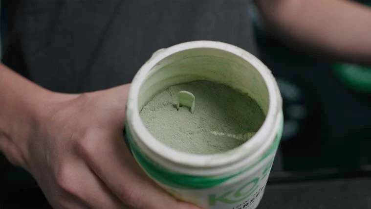 A container of KOS Greens Powder supplements.