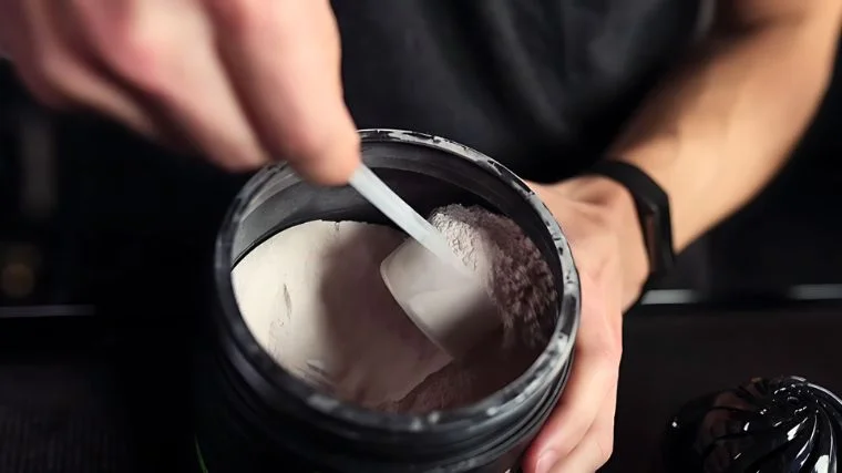 Protein powder benefits: This photo is of a hand scooping protein powder from a container.