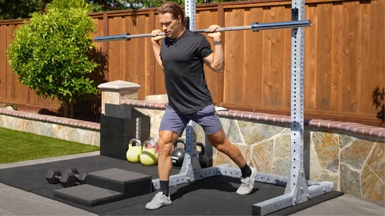 A person holding a barbell across his traps preparing to squat.