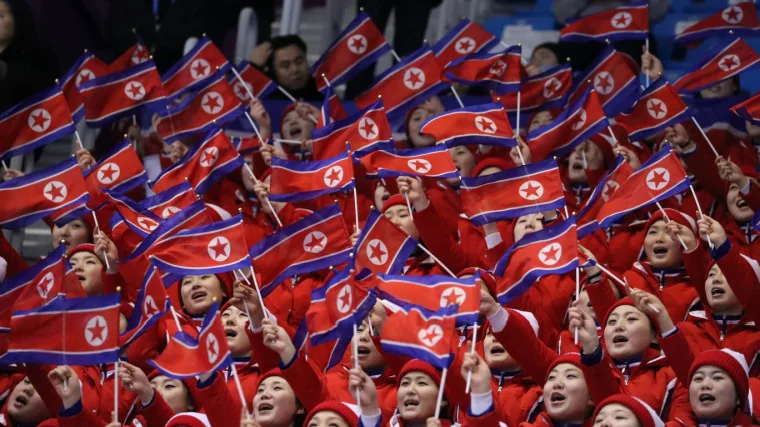 North Korean fans wave flags in stadium at athletic event.