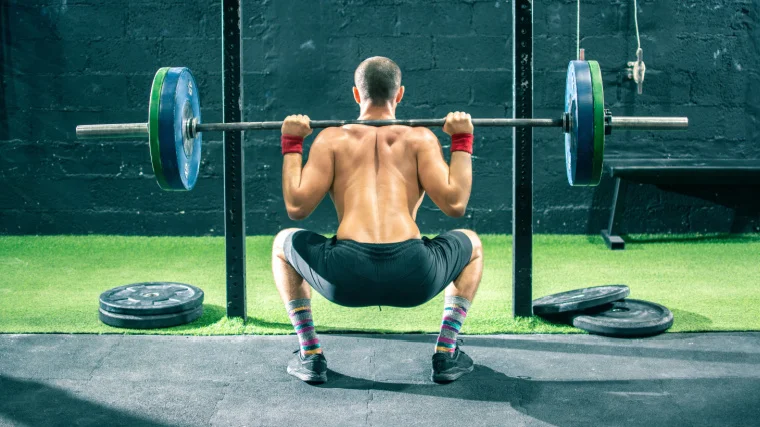 Back view of a sportsperson lifting a barbell in the gym.