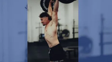Justin Medeiros lifts a barbell over his head.