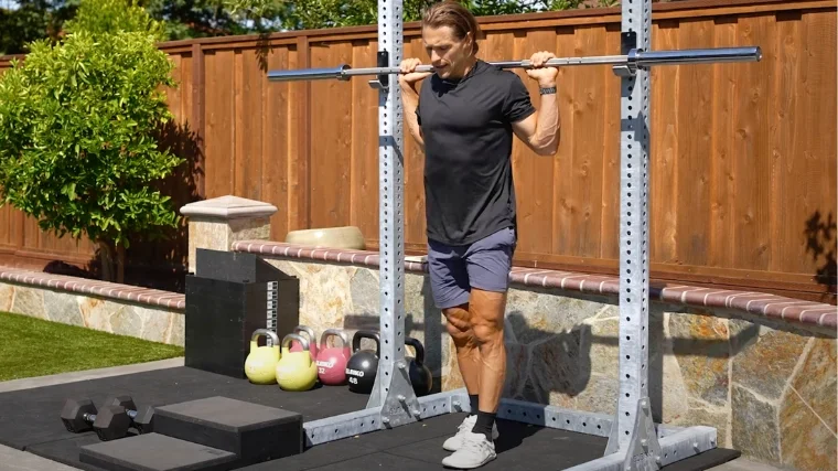 A person holding a barbell across his traps.