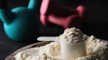 Protein powder in a scoop, with free weights in the background.