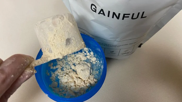 A person scoops out Gainful Vegan Protein from its bag.