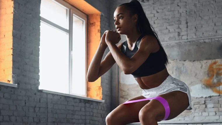 A confident young person using an elastic resistance band while exercising in the gym.