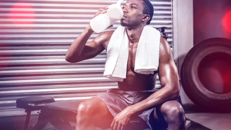 A person sits on a bench and drinks during a workout.
