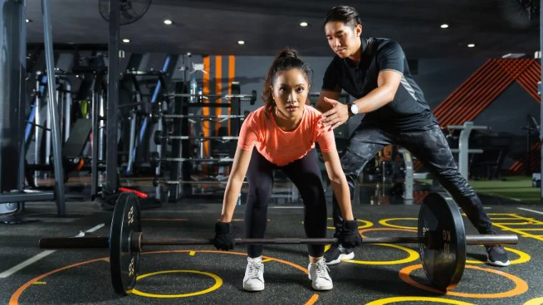 A beginner being coached on doing a deadlift.