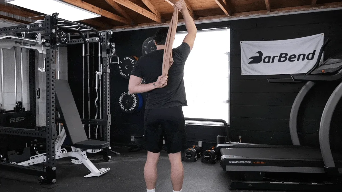 A person performing the assisted overhead tricep stretch exercise with a towel.
