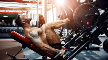 A shirtless athlete performs a heavy leg press.