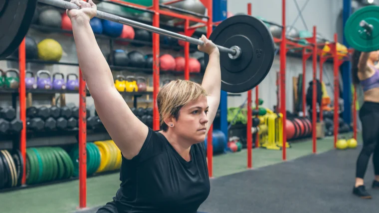 A person performs a barbell snatch in a colorful gym.