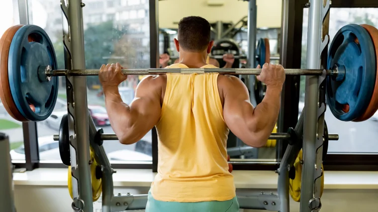 Back view of a sportsperson lifting a barbell in the gym.