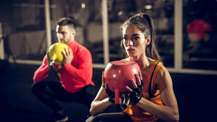 Two people lifting kettlebells while squatting in the gym