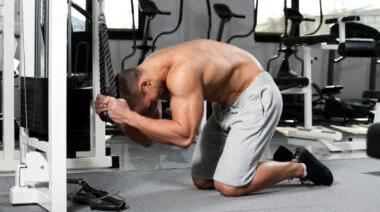 A shirtless person performs a cable crunch while facing the cable stack.